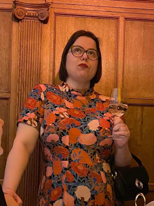 Bild på Elise klädd i en storblommig klänning i orange, rosa, rött och blått på svart bakgrund